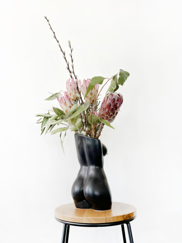 Black femme vase with nipple tassels back view filled with an arrangement of decorative protea and foliage