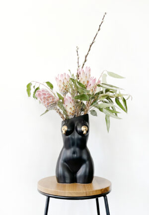 Black femme vase with nipple tassels filled with an arrangement of decorative protea and foliage