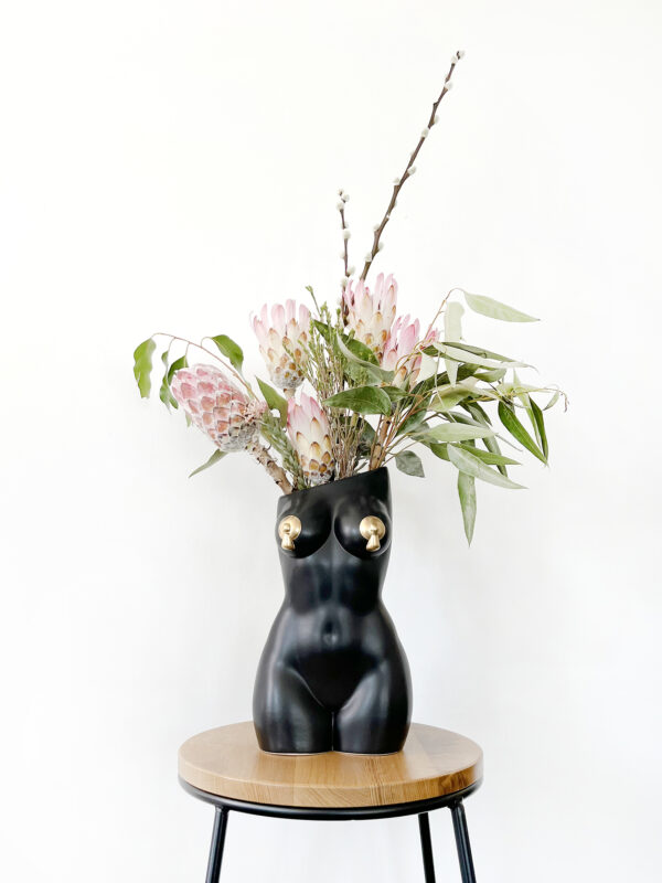 Black femme vase with nipple tassels filled with an arrangement of decorative protea and foliage