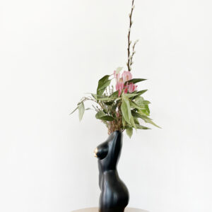 Black femme vase with nipple tassels side view filled with an arrangement of decorative protea and foliage