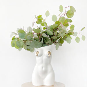 White femme vase with nipple tassels filled with an arrangement of decorative eucalyptus foliage