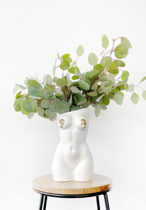 White femme vase with nipple tassels filled with an arrangement of decorative eucalyptus foliage